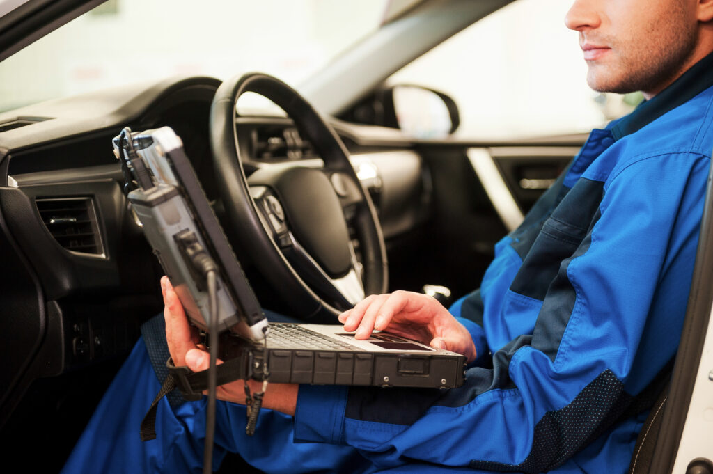 Man examining car. Confident young man working on special laptop while sitting in a car in workshop